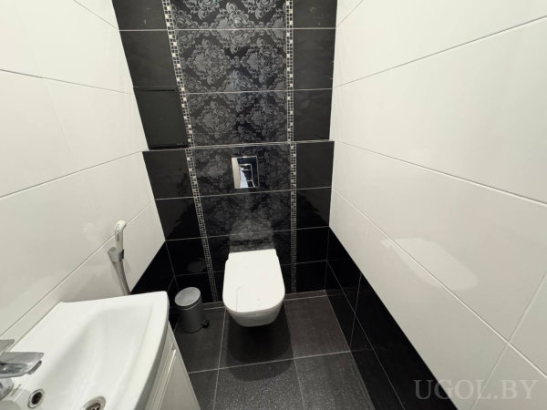 Компактная зона с унитазом, умывальником, мусоркой, глянцевой плиткой и декоративной панелью.