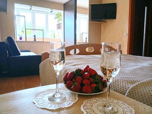 Уютная спальня с кроватью, столиком у окна, двумя бокалами и тарелкой свежей клубники.