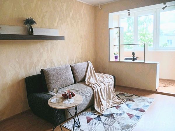 Светлая гостиная с серым диваном и пледом, на столике два бокала, клубника и шоколад.