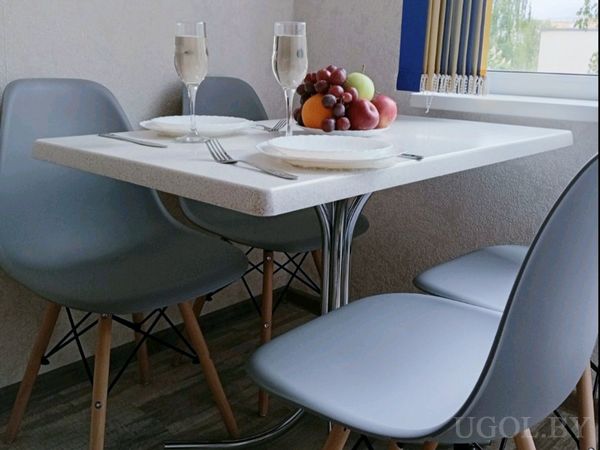 Белый обеденный стол с сервировкой на двоих, бокалами и фруктовой композицией в центре.