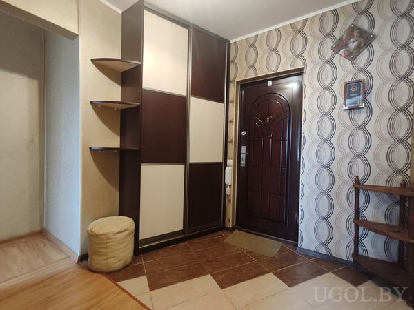 Коридор с тёмно-бежевым шкафом, круглым пуфом и входной дверью.