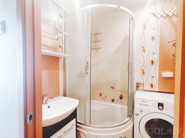 Компактная ванная с угловой душевой кабиной, раковиной и стиральной машиной.