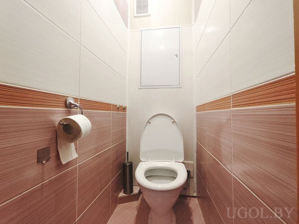 Небольшой санузел с унитазом, бело-коричневой плиткой и оранжевой декоративной полосой.