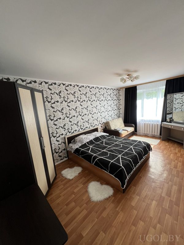 Комната с кроватью в геометричном текстиле, ковриками-сердцами, чёрно-белыми обоями и диваном у окна.