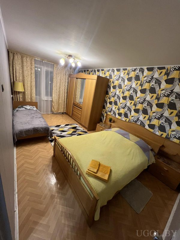 Комната с серой и жёлтой кроватями, зеркальным шкафом, ковром в тон и обоями с листьями и полосами.