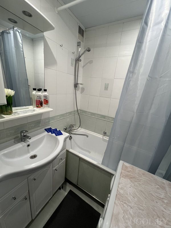 Ванная с умывальником, цветами, косметикой Dalie и бело-зелёной плиткой.