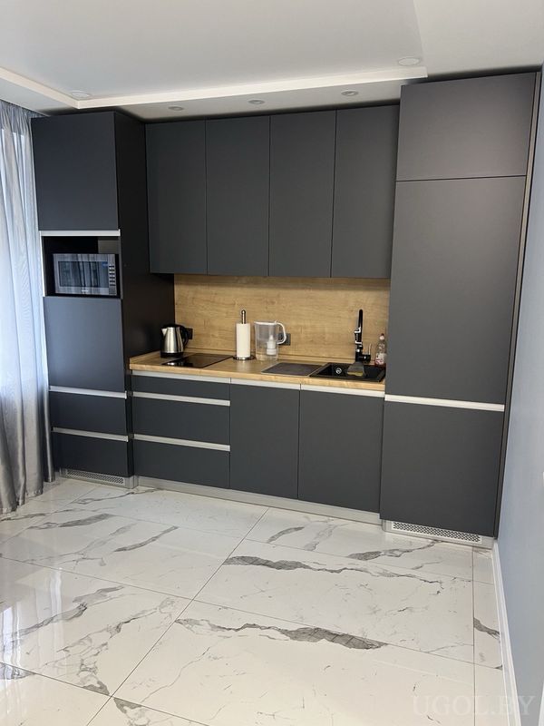 Современная кухня с серыми шкафами, деревянной столешницей, чёрным краном и техникой на фоне мраморного пола.