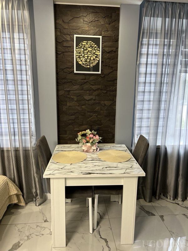 Уютный уголок с мраморным столом, двумя тёмными стульями, вазой с цветами и панно с золотыми рыбами.