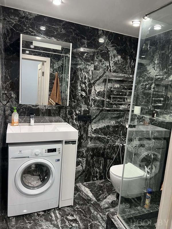 Функциональная ванная с мраморной плиткой, душевой кабиной, стиральной машиной и умывальником с зеркалом.
