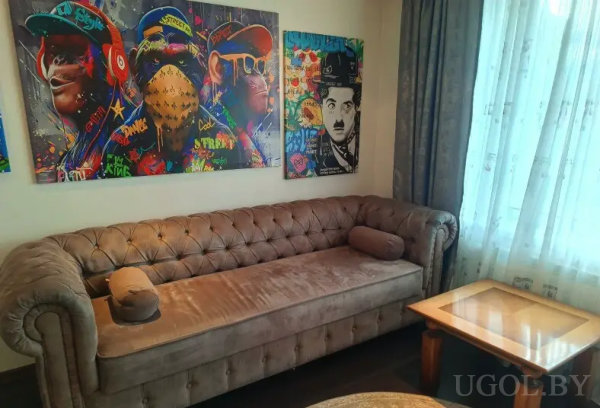 Уютный уголок с бежевым диваном и яркими картинами в стиле граффити, включая образ «Чарли Чаплина» и обезьян в очках.