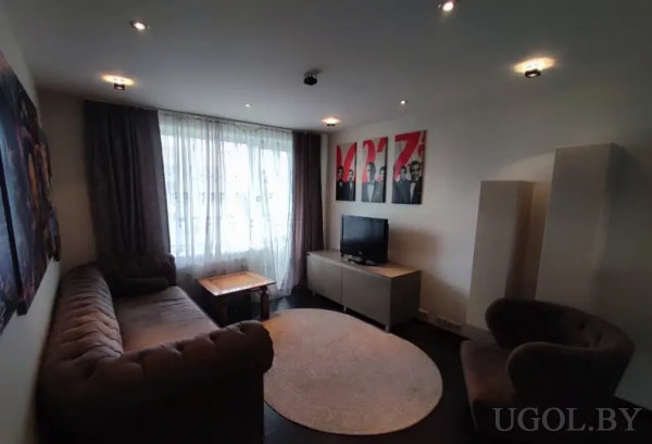 Теплый интерьер с мягкой мебелью, телевизором и тремя постерами с графичными портретами на красном фоне.