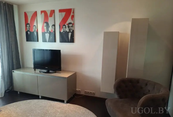 Комната с темным креслом, светлой тумбой под ТВ и тремя картинами с мужчинами в костюмах на фоне красных фигур.