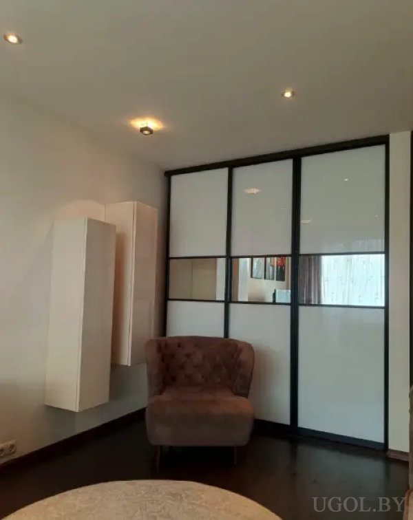 Современное пространство с коричневым креслом, белым шкафом с зеркальными вставками и настенными шкафами.