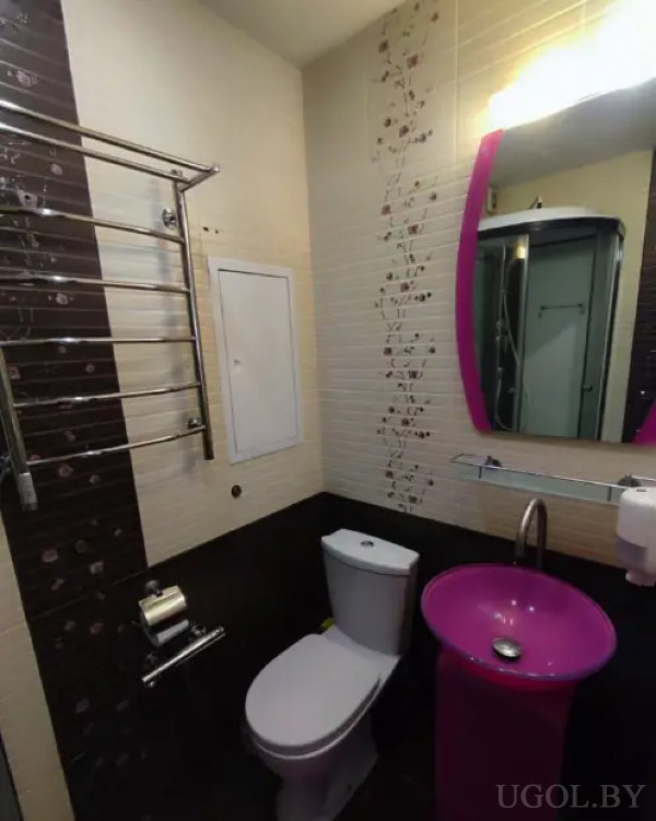 Яркая ванная с розовой раковиной, зеркалом в тон и настенным полотенцесушителем на фоне плитки с цветочным узором.