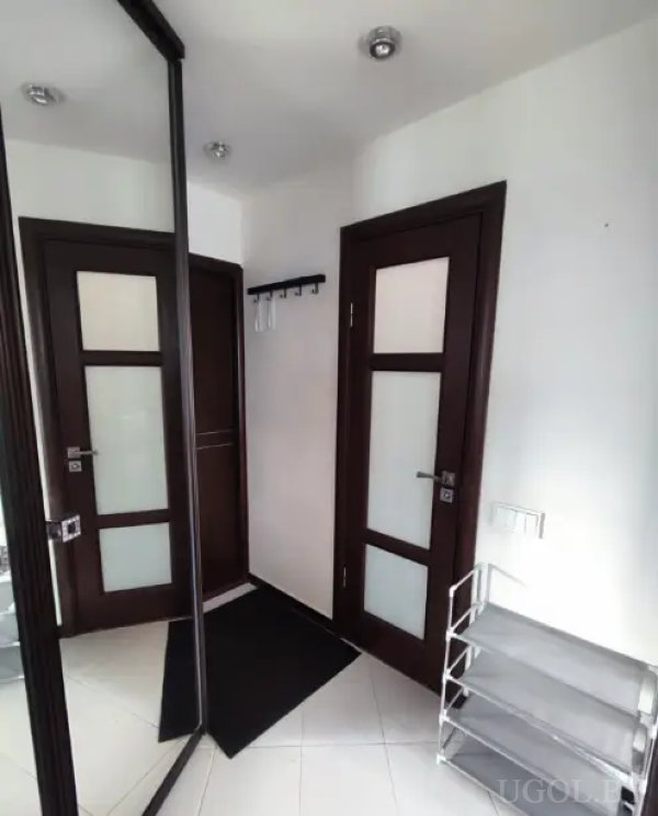 Минималистичный коридор с двумя дверями, настенной вешалкой, зеркалом и металлической обувницей на фоне светлой плитки.