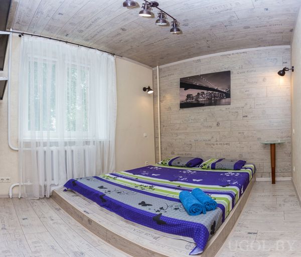 Современная спальня с низкой кроватью на подиуме, ярким покрывалом с бабочками и большим окном с белыми шторами.