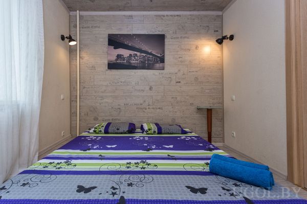 Небольшая спальня с кроватью в ярком покрывале с бабочками, настенными лампами и фотографией ночного города.