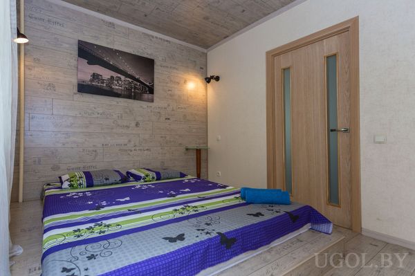 Минималистичная спальня с кроватью в ярком покрывале, деревянными стенами и фотографией моста на стене.