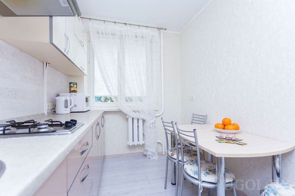 Компактная кухня с плитой, микроволновкой, чайником и небольшим столом с четырьмя стульями.