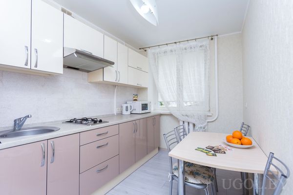 Современная кухня с бежевыми и коричневыми шкафами, плитой, мойкой и столом с апельсинами.