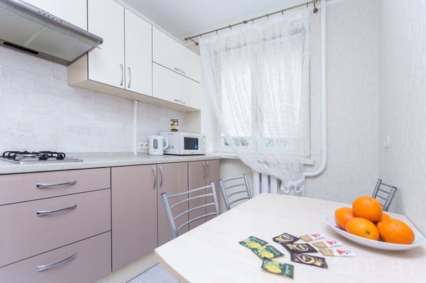 Светлая кухня с белыми шкафами, плитой, чайником и столом с фруктами и пакетиками чая.