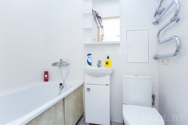 Небольшая ванная с белой ванной, раковиной, унитазом и настенным полотенцесушителем.