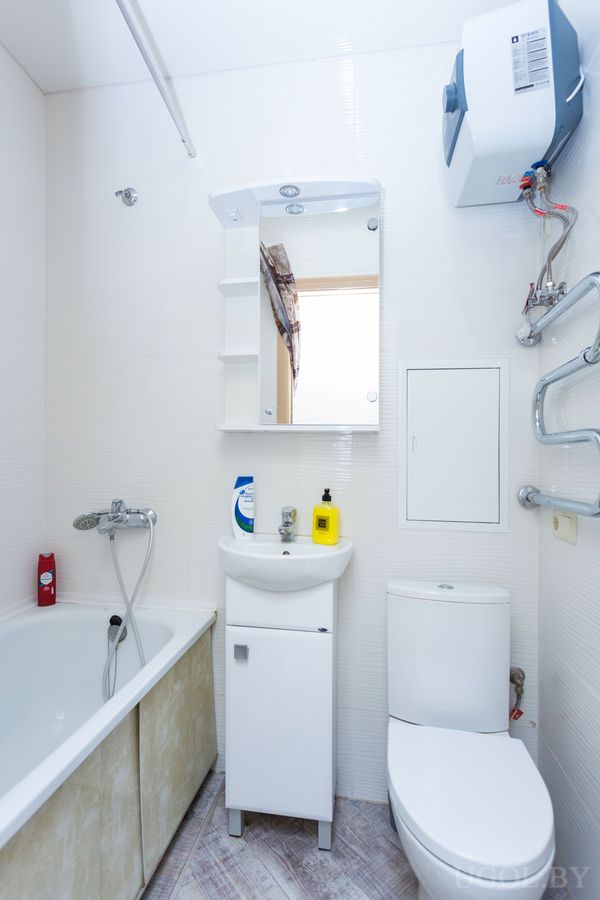 Компактная ванная с белой ванной, раковиной, унитазом и настенным водонагревателем.