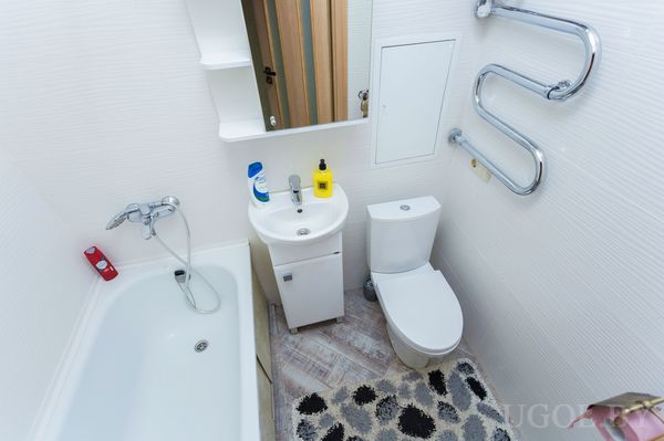 Небольшая ванная с белой ванной, унитазом, раковиной и ковриком с узором.