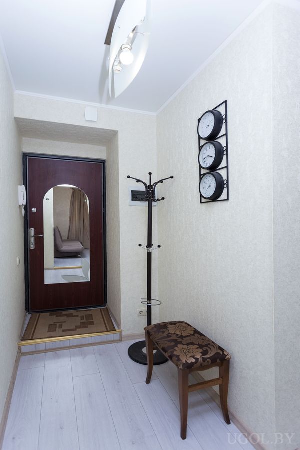 Небольшая прихожая с зеркальной дверью, вешалкой, пуфом и часами в ряд на стене.