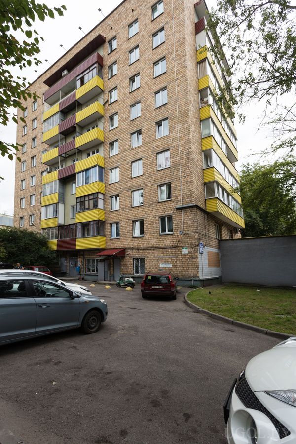 Многоэтажный жилой дом с цветными балконами и парковкой перед зданием.
