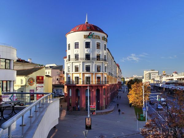 Городская улица с домом в красно‑белых тонах, круглой башней с куполом и вывеской пиццерии.