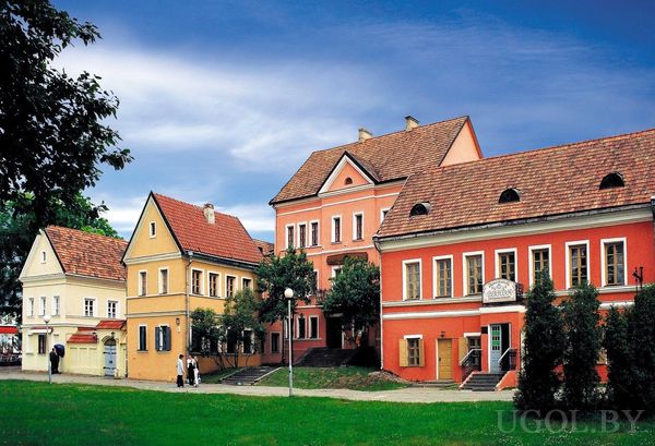 Живописная улица с красными и жёлтыми историческими домами с черепичными крышами и зеленью вокруг.