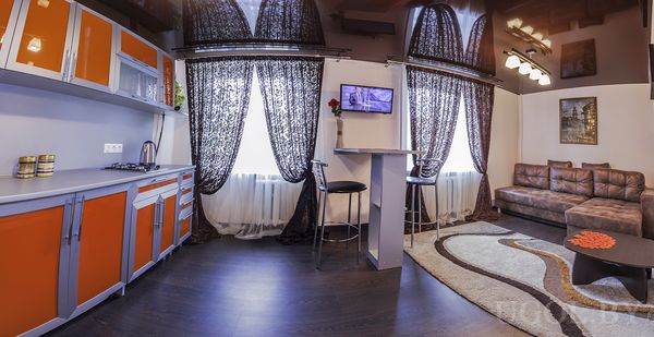 Современная квартира-студия с компактной кухней, барным столом, ТВ на стене и уютной зоной отдыха у окна.