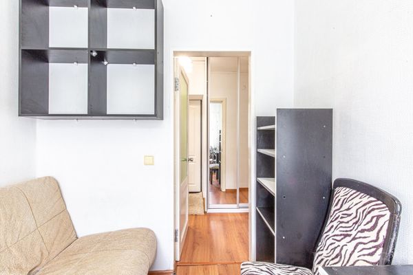 Небольшая комната с бежевым диваном, чёрным книжным шкафом, кубической полкой и креслом с зебровым узором.