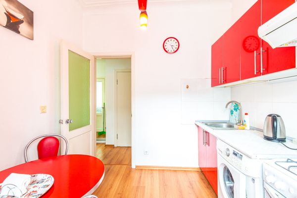 Современная кухня с красными шкафами, мойкой, стиральной машиной и круглым красным столом со стулом.