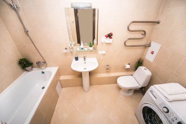 Белая ванна с душем, раковина с зеркалом и принадлежностями, унитаз с полотенцесушителем над ним, стиральная машина с полотенцем сверху.