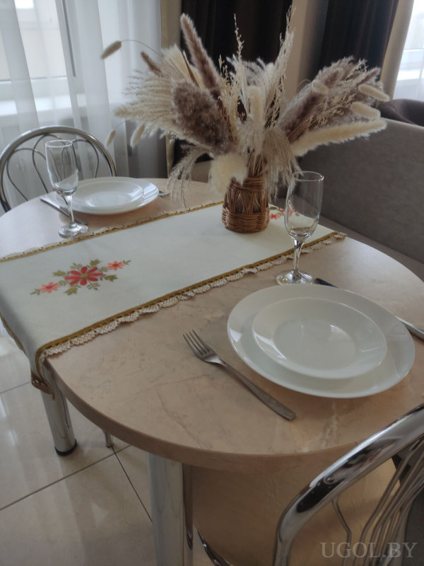 Круглый стол с мраморной столешницей, сервировка на двоих, декоративная салфетка и ваза с сухоцветами, на фоне тюль и тёмные шторы.