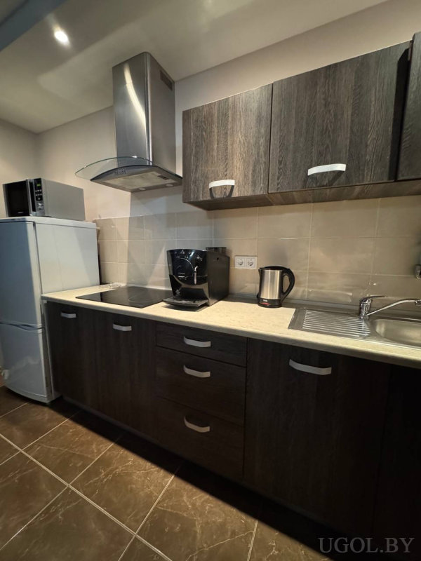 Вытяжка над плитой, кофемашина, чайник, раковина, холодильник с микроволновкой, тёмная плитка пола и светлый фартук.