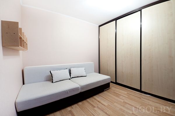 Светлая комната с угловым диваном, встроенным шкафом‑купе и розовыми стенами.