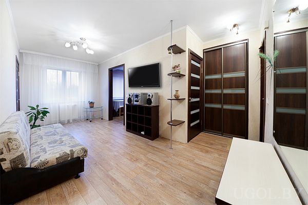 Современная гостиная с диваном, телевизором на тумбе, полкой с декором и шкафами с матовым стеклом.