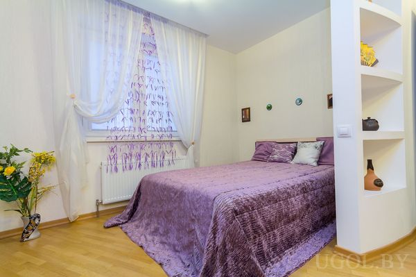 Комната с кроватью, вазой, шторой, полками, декором и светлым полом.