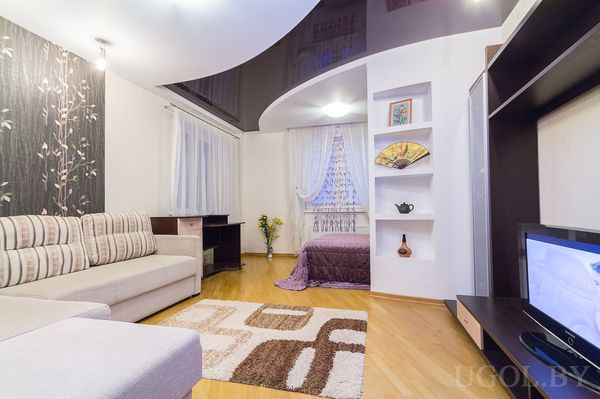 Комната с диваном, ковром, телевизором, тюлем, столом и декоративной отделкой.