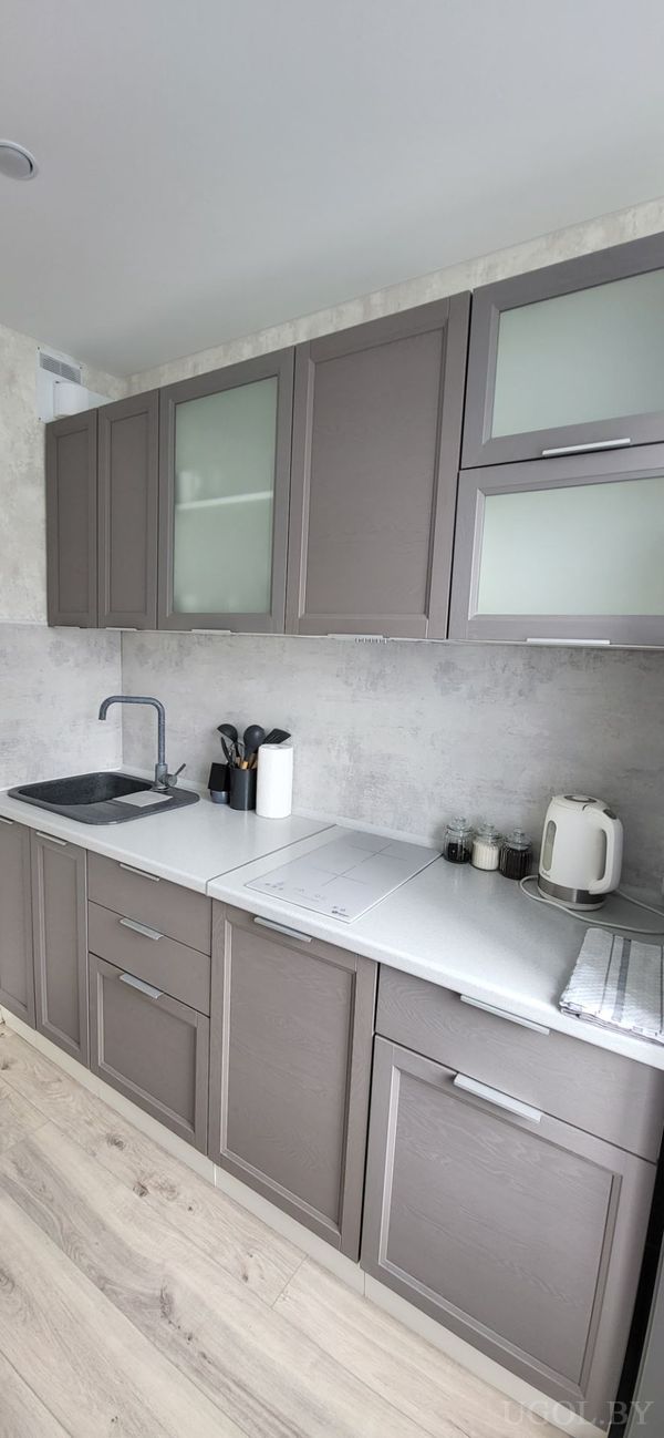 Кухонная зона с серыми шкафами, белой плитой, чайником, набором специй и стеклянными верхними фасадами.