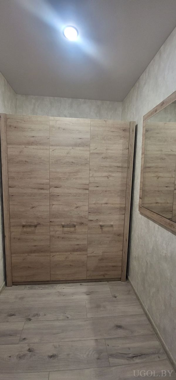 Интерьер с деревянным шкафом, зеркалом в раме, точечным светом и отделкой в светлых тонах.