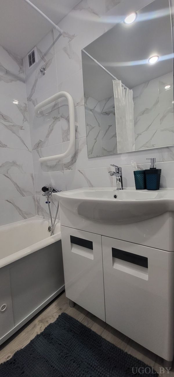 Комната с ванной, умывальником, зеркалом, мраморной плиткой и ковриком на полу.