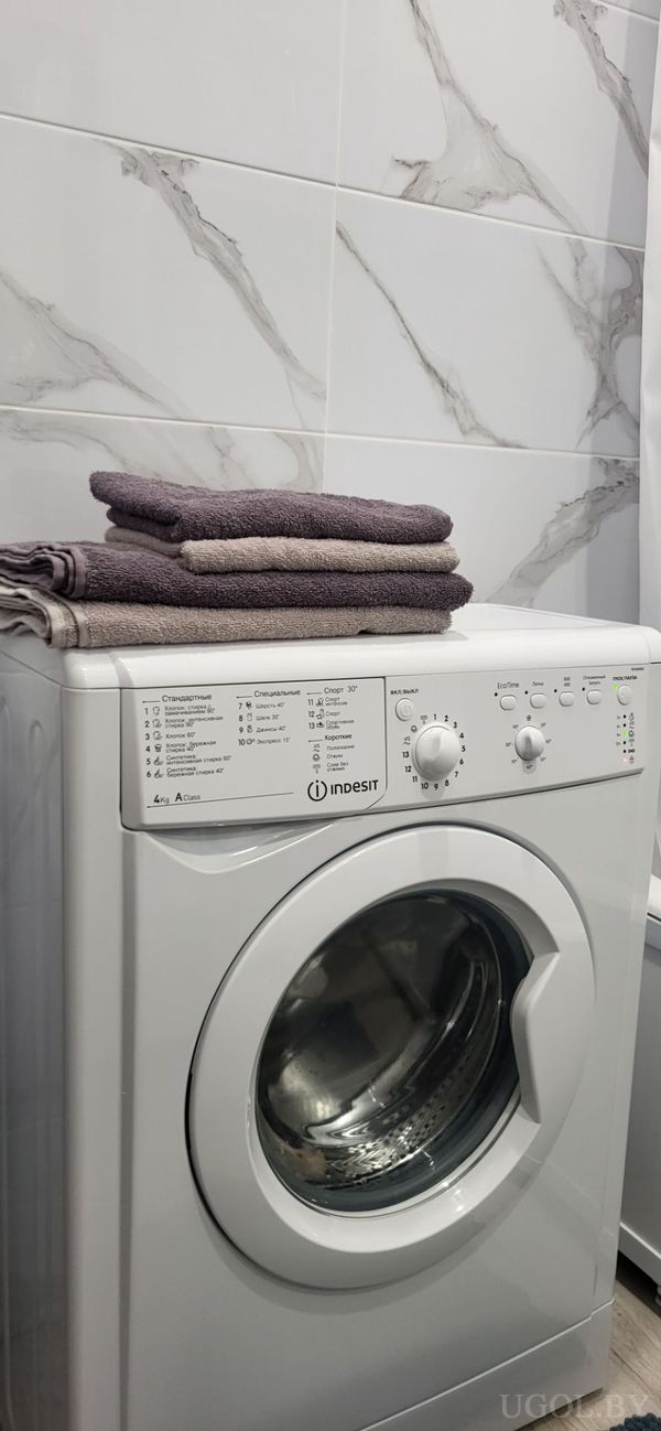 Машина с панелью на русском языке, стопкой серых и бежевых полотенец и плиткой с мраморным рисунком.