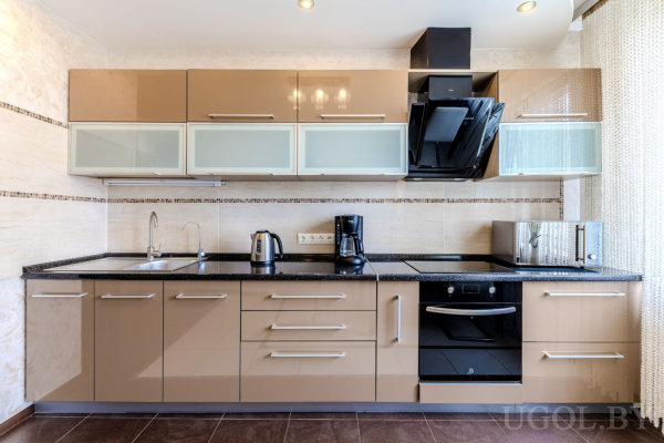 Кухня с бежевыми шкафами, чёрной столешницей, мозаичным фартуком, встроенной техникой и бытовыми приборами на рабочей поверхности.