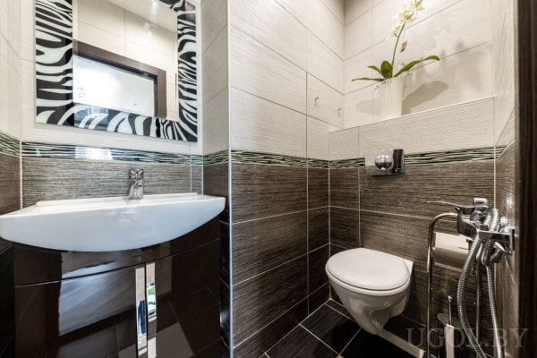 Компактный санузел с тёмной тумбой, зеркалом в зебровой раме, настенным унитазом, мозаичной полосой и нишей с орхидеей.