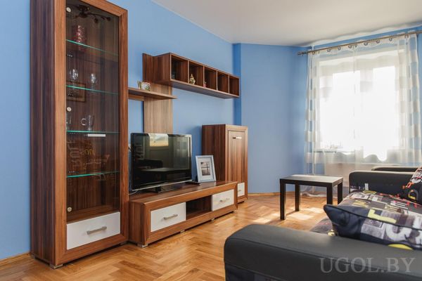 Синяя стена, бело-коричневая мебель, телевизор, стеклянный шкаф, шторы и журнальный столик.