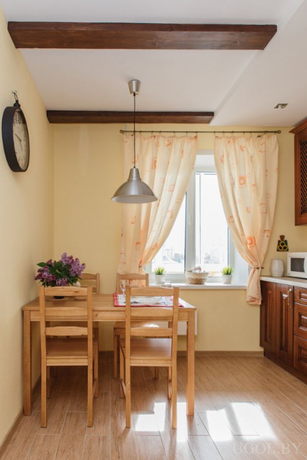Жёлтые стены, деревянный стол на четыре персоны, фиолетовые цветы, часы и открытые балки на потолке.
